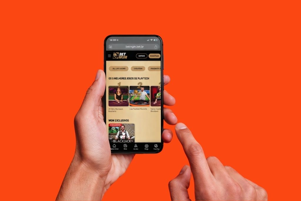 Mãos segurando um celular que exibe o site da BetMGM com uma lista intitulada os 5 melhores jogos de Playtech Cassino em destaque na tela do dispositivo sobre um fundo laranja.