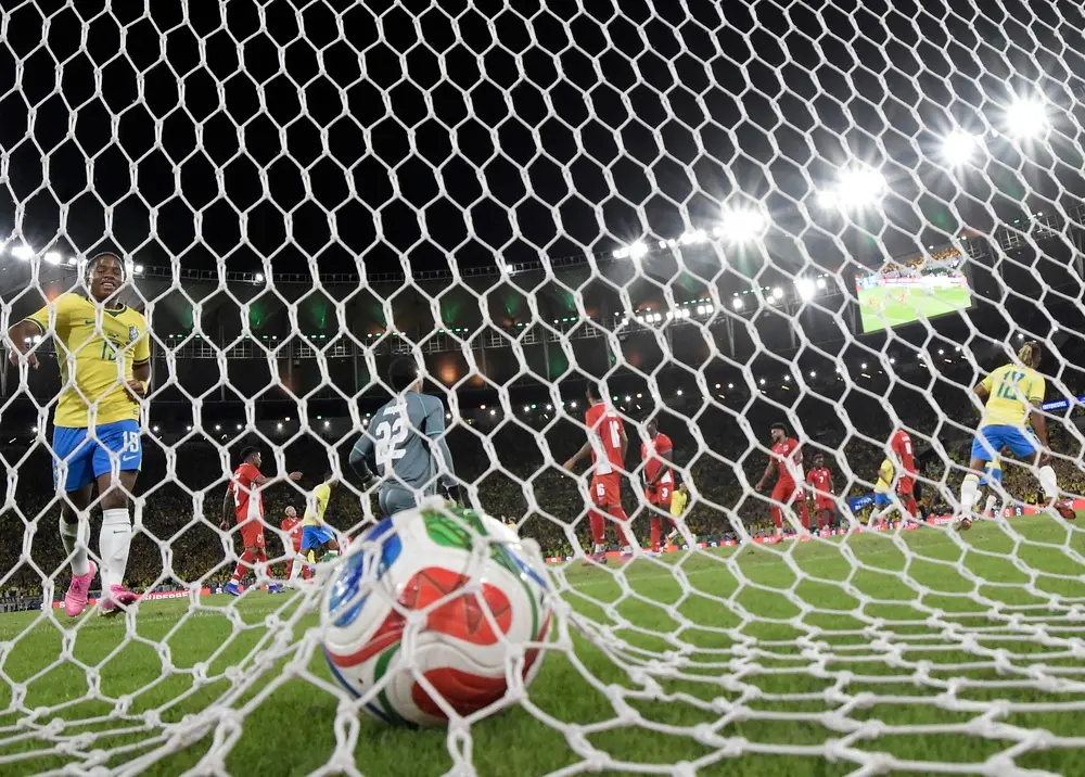 Bola da Copa do Mundo dentro do gol após lance decisivo em partida da Seleção Brasileira, com jogadores em campo e estádio iluminado ao fundo, ilustrando o cenário de apostar nos favoritos da Copa do Mundo.